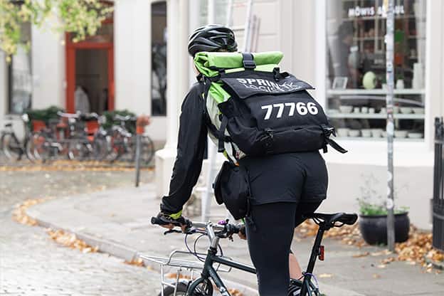 Eine Kurierin auf dem Fahrrad mit dem Sprint Logistik Rucksack wo die Rufnummer 77766 prominent zu sehen ist.